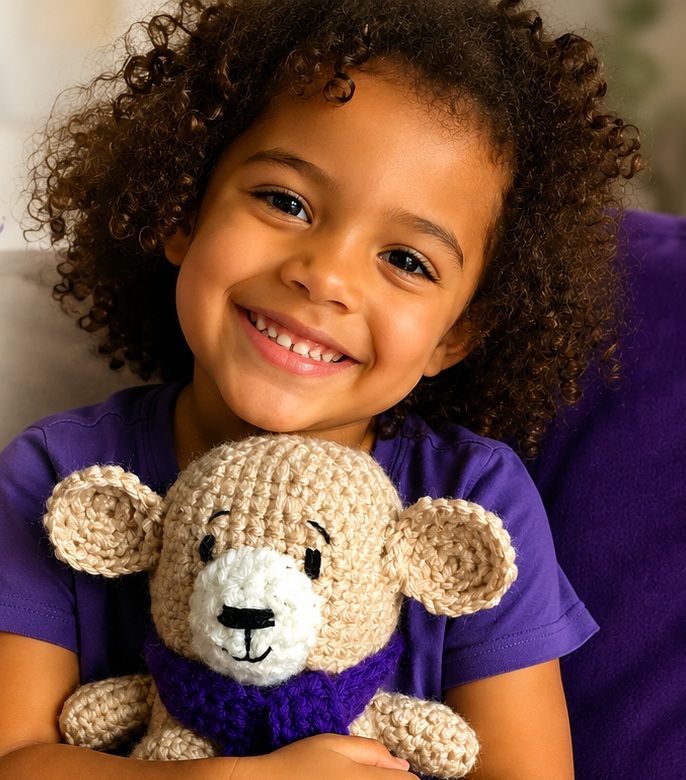 A smiling child holding a handmade HOPE Bear